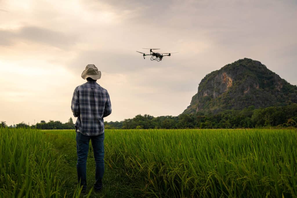 A farmer operating a drone over an open grass field with a mountain in the background